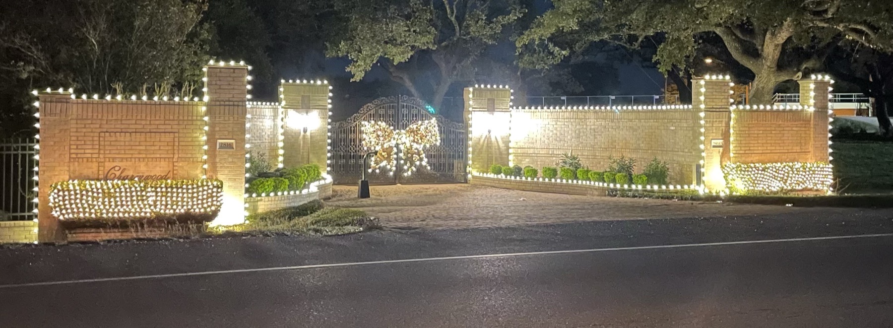Neighborhood entry wall, pillars and gate outlined in warm white Christmas lights