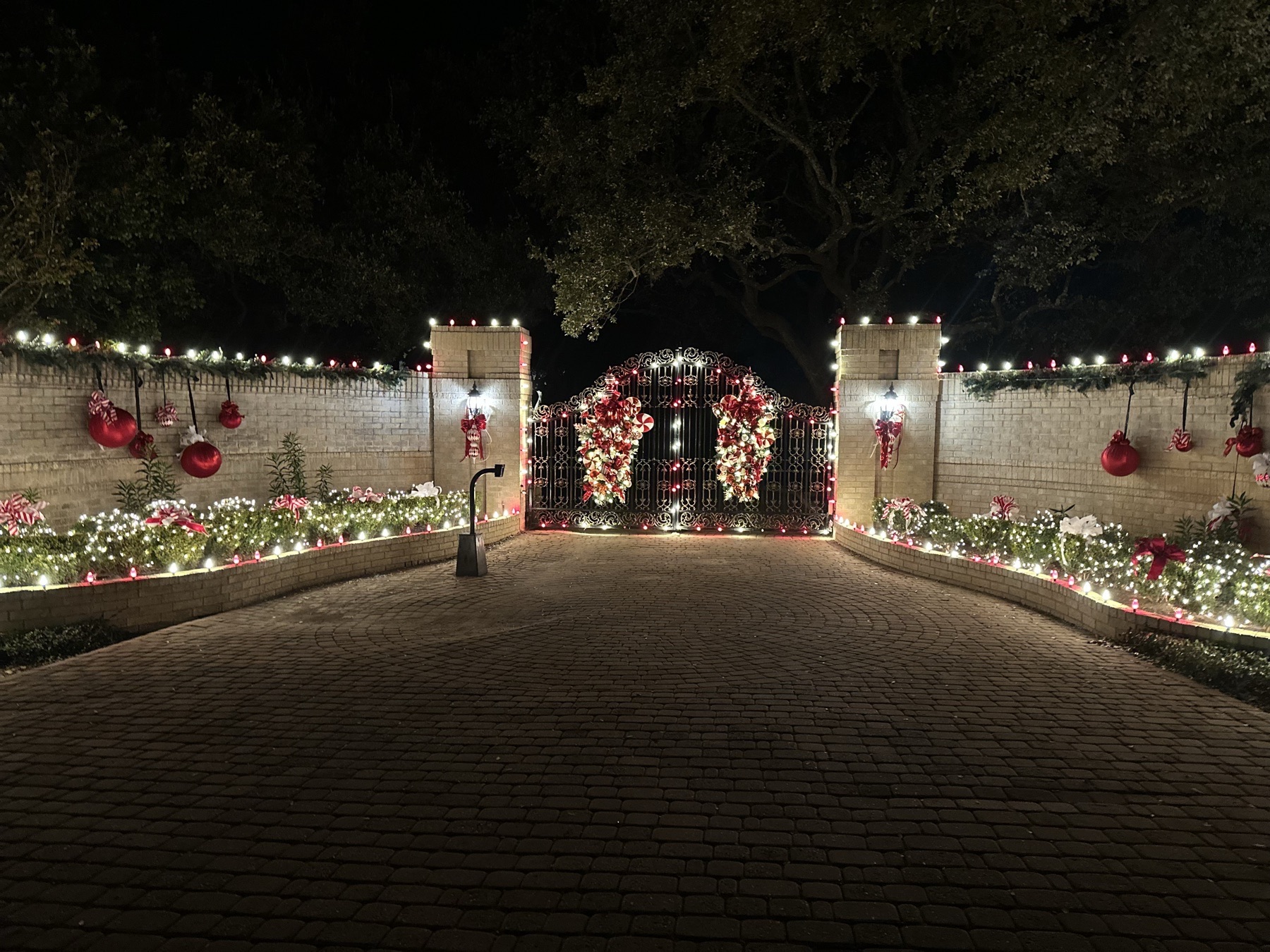 Gated driveway lined with red and warm white Christmas lights, garland and ornaments