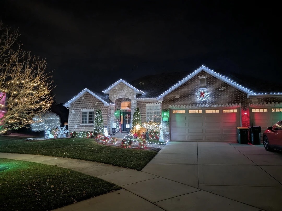 Front elevation of a home with lit roofline, columns and landscape accents